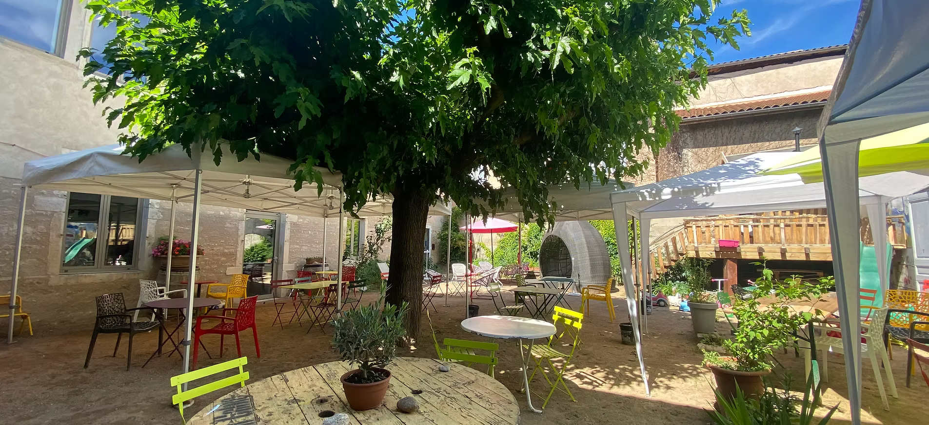 Photo de la cour intérieure terrasse, avec un arbre central, des barnums, des tables et chaises